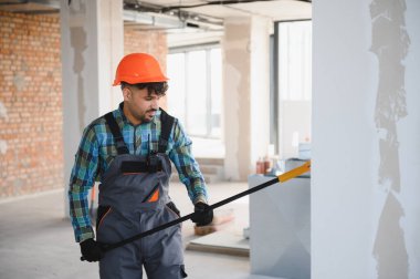 Arap müteahhit, yoğun bir inşaat alanındaki duvardaki sıvaları kontrol etmek için uzun bir araç kullanıyor, kalite kontrolü ve hassasiyete odaklanıyor.