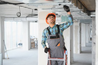 Arap mühendis inşaat sahasına tavan yapısı kuruyor, merdiven üzerinde çalışıyor ve tornavida kullanıyor.