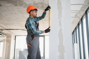 Arap mühendis tulum ve şapka giyer, hareketli bir inşaat alanında ölçüm yaparken hassasiyeti sağlamak için ruh seviyesini kullanır.