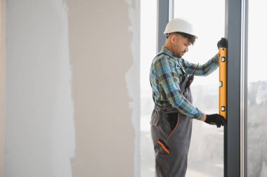 Yoğun bir inşaat sahasına yeni bir pencere kurarken tam hizalama için ruh seviyesini kullanan konsantre yapıcı