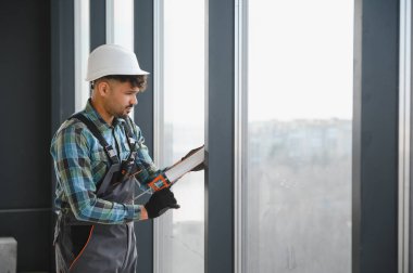 Arap inşaat işçisi silikon dolgu maddesi sürerken modern yüksek binaların camlarını yerleştiriyor, marifetli işçilik sergiliyor.