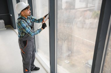 Arap müteahhit, hava geçirmez ve hava geçirmez bir kurulum sağlamak için inşaat alanındaki büyük bir pencere iskeletine dolgu macunu sürüyor.