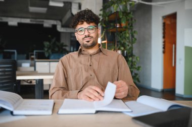 Genç Arap öğrenci kitap okuyor ve modern bir üniversite kütüphanesinde notlar alıyor, sınavlara hazırlanıyor ve yeni kavramlar öğreniyor.