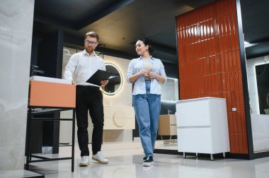 Satıcının elinde banyo armatürleri ve seramik fayansları gösteren bir pano var.