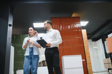 Parlak, modern bir perakende mağazası ortamında seramik fayanslar ve su tesisatı seçeneklerini sergileyen bir müşteri danışmanı