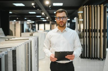 Seramik fayans ve tesisat dükkanında çalışan satıcı, envanteri kontrol ediyor ve müşterilere yardım ediyor.