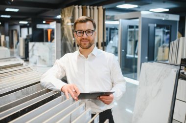 Satıcının elinde bir pano var. Seramik seramik seramik seramik seramik koleksiyonu parlak, modern bir hırdavatçıda müşteriye sunuyor.