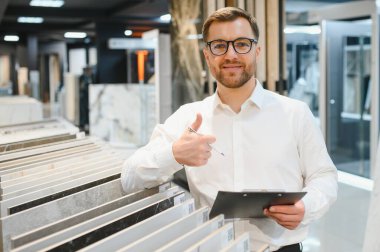 Satıcının elinde bir pano, parlak ve organize seramik seramik ve su tesisatı ürünlerini sergiliyor.