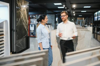 Satış elemanı elinde seramik fayansları hırdavatçıdaki kadın müşteriye gösteriyor. Satın almayı tartışıyorlar.
