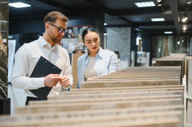 Satıcının elinde seramik fayans örneklerini gösteren bir pano var. Tesisat ve seramik dükkanındaki kadın müşteriye.