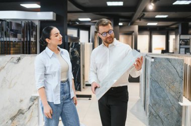 Satıcı, iyi organize edilmiş bir tesisat ve kiremitçide kadın bir müşteriye seramik fayans sunuyor. Seçenekleri ve seçenekleri tartışıyor.