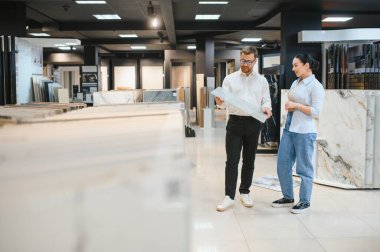 Satış elemanı bir müşteriyle görüşüyor, seramik ve su tesisatı mağazalarında çeşitli fayans seçenekleri sunuyor, kalite ve tarz seçimlerini vurguluyor.