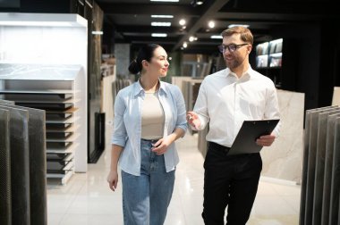 Satıcının elinde seramik fayansları gösteren bir pano var. Tesisat ve fayans mağazalarının galerisinde yürüyor.