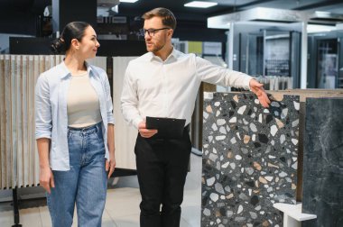 Seramik ve sıhhi tesisat dükkanında çalışan bir kadına farklı seramik fayanslar gösteren profesyonel bir tezgahtar.