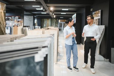 Modern bir hırdavatçıda kadın müşteriye farklı seramik örnekler sunan satıcı yenileme projesi için doğru malzemeyi tartışıyor ve seçiyor.