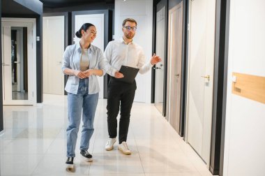 Profesyonel mağaza asistanı pano tutuyor ve hırdavatçıda yürüyen kadın müşterilere iç kapılar gösteriyor.