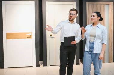 Profesyonel satıcı mobilya mağazasında kadın müşteriye farklı kapı modelleri gösteriyor, özellikleri tartışıyor ve doğru seçimi yapmasına yardım ediyor.