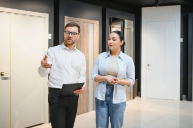 Hırdavatçı dükkanında kadınlara çeşitli modern kapılar gösteriyor, karakteristik özellikleri tartışıyor ve seçmesine yardım ediyor.