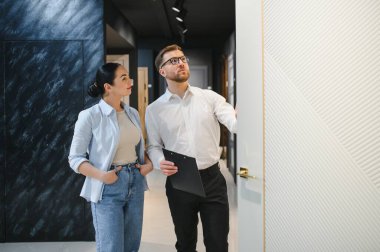 Profesyonel mağaza asistanı seramik fayans ve tesisat mağazasında pano tutan modern beyaz kapıyı bayan müşteriye gösteriyor.