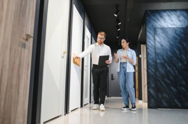 Kadın müşteri, modern bir fayans ve su tesisatı mağazasında bir erkek satış elemanıyla çeşitli tasarım seçeneklerini tartışıyor.