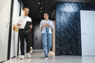 Satıcının elinde pano var. Seramik fayans ve su tesisatı mağazasında yürüyen müşteriye farklı kapılar gösteriyor.