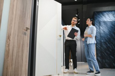 Satıcı hırdavatçıda bir kadına farklı kapılar gösteriyor. Doğru kapıyı seçmesine yardım ediyor.