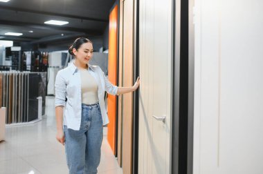 Kadın, bilgili bir satıcının rehberliğinde seramik fayansları inceliyor. Parlak galeride çeşitli ev geliştirme malzemeleri sergileniyor.