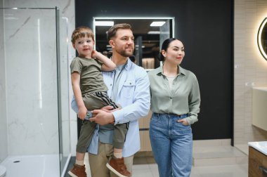 Aile seramik fayansları ve banyo demirbaşlarını bir su tesisatçısında seçiyor, baba oğlunu kucağında tutuyor.