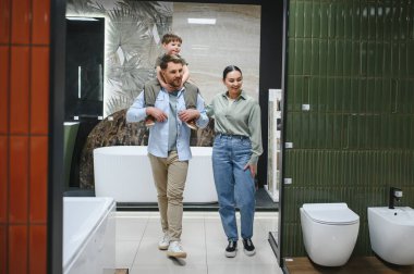 Mutlu bir aile, oğullarını omuzlarında taşıyarak bir tesisat dükkanında seramik fayanslar ve banyo demirbaşlarını seçiyor.