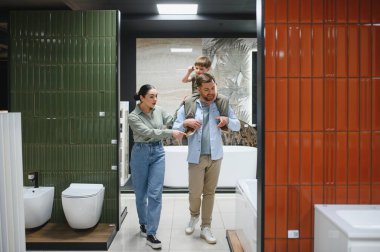 Çocuklarıyla birlikte seramik fayans ve su tesisatını ziyaret eden çift, çeşitli banyo armatürlerini ve ev dekorasyonu seçeneklerini inceliyor.