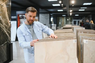 Hırdavatçıda seramik fayanslar seçen, numunelere dokunan ve yenileme projesi için mükemmel malzemeyi arayan bir adam.