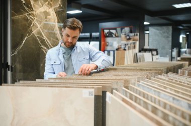 Adam seramik fayansları, çeşitli fayans seçenekleri ve tesisat armatürleriyle çevrili çağdaş bir mağazada inceliyor.