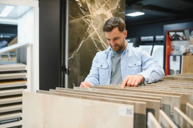 Bir adam, yenileme projesi için farklı örnekler karşılaştırarak, bir ev geliştirme mağazasından seramik fayanslar seçiyor.