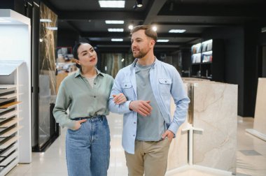 Seramik fayans ve su tesisatı dükkanında yürüyen çift, ev yenileme seçeneklerini tartışıyor. Seçimle ilgili ve ilgili görünüyorlar.