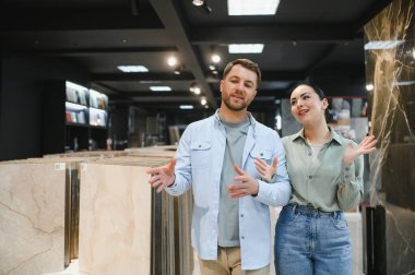 Bir çift, bir mağazada satış asistanıyla seramik fayans seçeneklerini tartışıyor ve evleri için yenileme kararları alıyor.