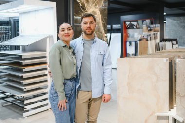 Çift, modern bir hırdavatçıda dairelerini yenilemek için seramik fayanslar seçerken sarılıyor.