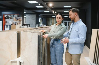 Çift, bir tesisat ve fayans dükkanındaki çeşitli seramik fayansları inceleyerek, ev yenileme projelerinin seçeneklerini tartışıyor.