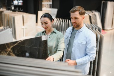 Hırdavatçı galerisinde seçenekleri tartışan çift, dairelerini yenilemek için çeşitli seramik fayanslara göz atıyorlar.