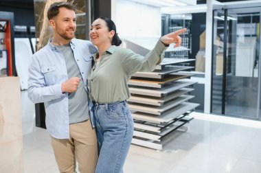 Modern bir hırdavatçıda banyo veya mutfak tadilatı için alışveriş yaparken seramik fayans örneklerini gösteren mutlu çift.
