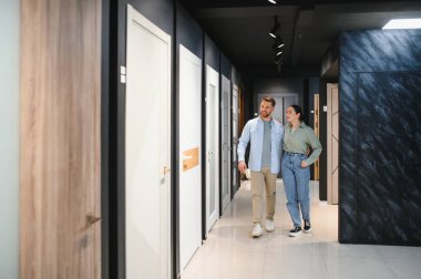 Mutlu çift canlı bir mobilya mağazasında el ele yürüyorlar, hayallerindeki ev için şık iç kapılar seçiyorlar.