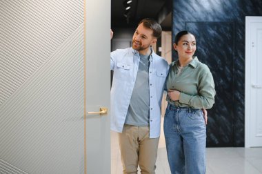 Mutlu çift inşaat malzemeleri dükkanında yeni bir iç kapı seçiyor, birbirlerini kucaklıyor ve neşeli gülümsemelerini paylaşıyorlar.