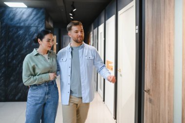 Genç bir çift hırdavatçıya gidiyor, yeni evleri için iç kapılar seçiyor, stil ve yenileme projelerini tartışıyorlar.