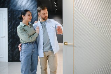 Mutlu çift mobilya ve nalbur dükkanında yeni bir iç kapı seçiyor kucaklaşıp gülümsüyor, kapıya dokunuyor.