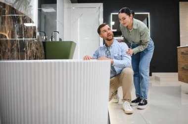 Genç bir çift, banyo mobilyası mağazasında yeni bir küvet seçiyor. Ev yenileme projelerini tartışıyor ve planlıyorlar.