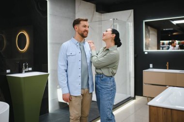 Modern bir galeride banyo eşyalar seçen mutlu çift lavabolara, duşlara ve diğer banyo unsurlarına hayran kalıyor.