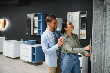 Mutlu çift banyo mobilyaları mağazasında modern duş kaplamasını seçiyor, yenileme planları yapıyor ve birlikte alışveriş deneyiminin tadını çıkarıyor.