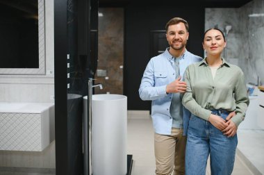 Mutlu çift modern bir tesisat dükkanında seramik fayanslar ve banyo demirbaşlarını seçiyor, gülümsüyor ve ev yenileme projeleri için ilham arıyorlar.