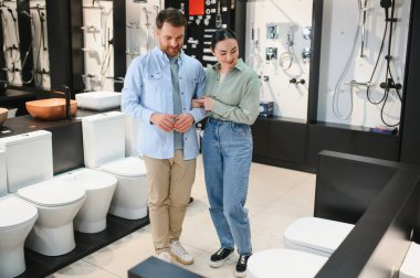 Çift, modern tuvalet ve duş başlıkları ile çevrili bir galeride modern banyo demirbaşlarını inceliyor ve ev yenileme fikirleri sergiliyor.