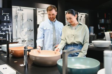 Çift modern bir seramik fayans ve tesisat dükkanında banyo lavabolarını ve demirbaşlarını inceliyor.