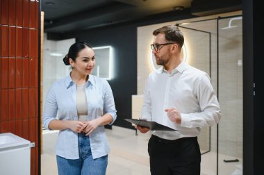 Satıcının elinde modern bir sergi salonundaki müşteriye banyo armatürlerini ve fayanslarını gösteren bir pano var.
